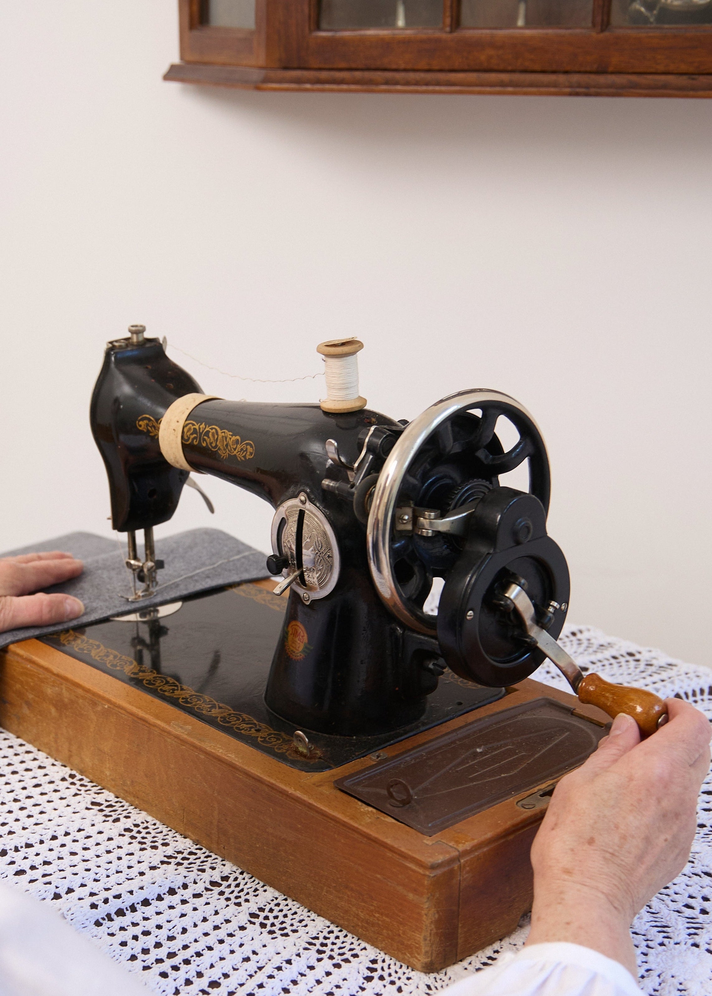 Person using an old-fashioned sewing machine at a table with a lace tablecloth.
