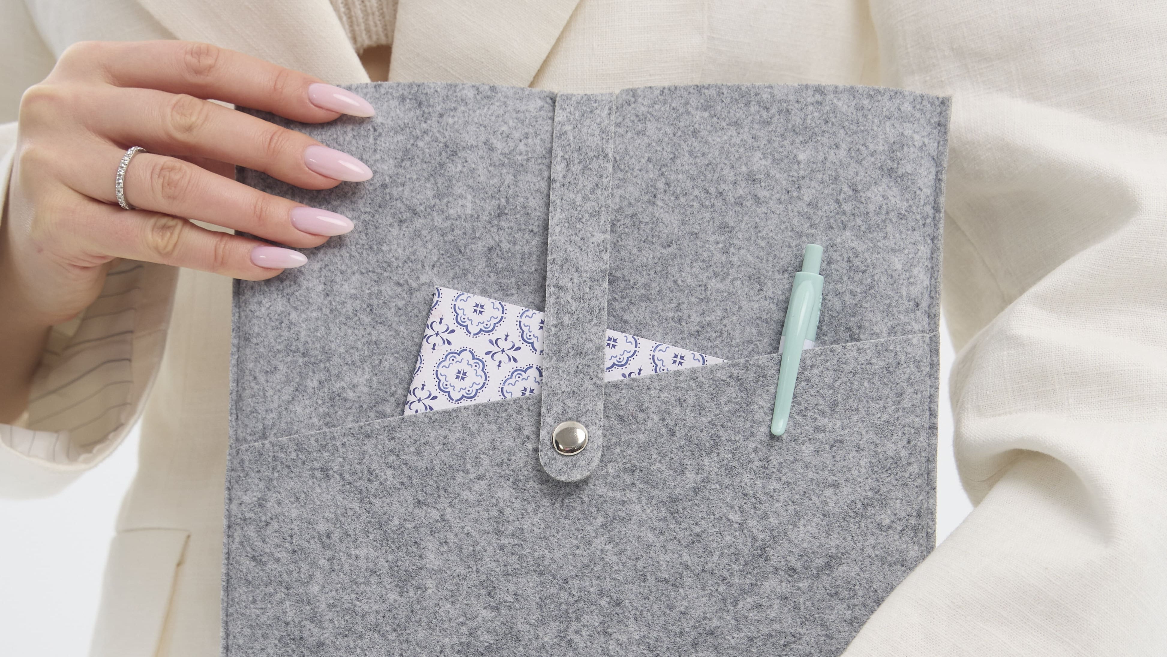 Person holding a gray felt pouch with a button closure on a white background
