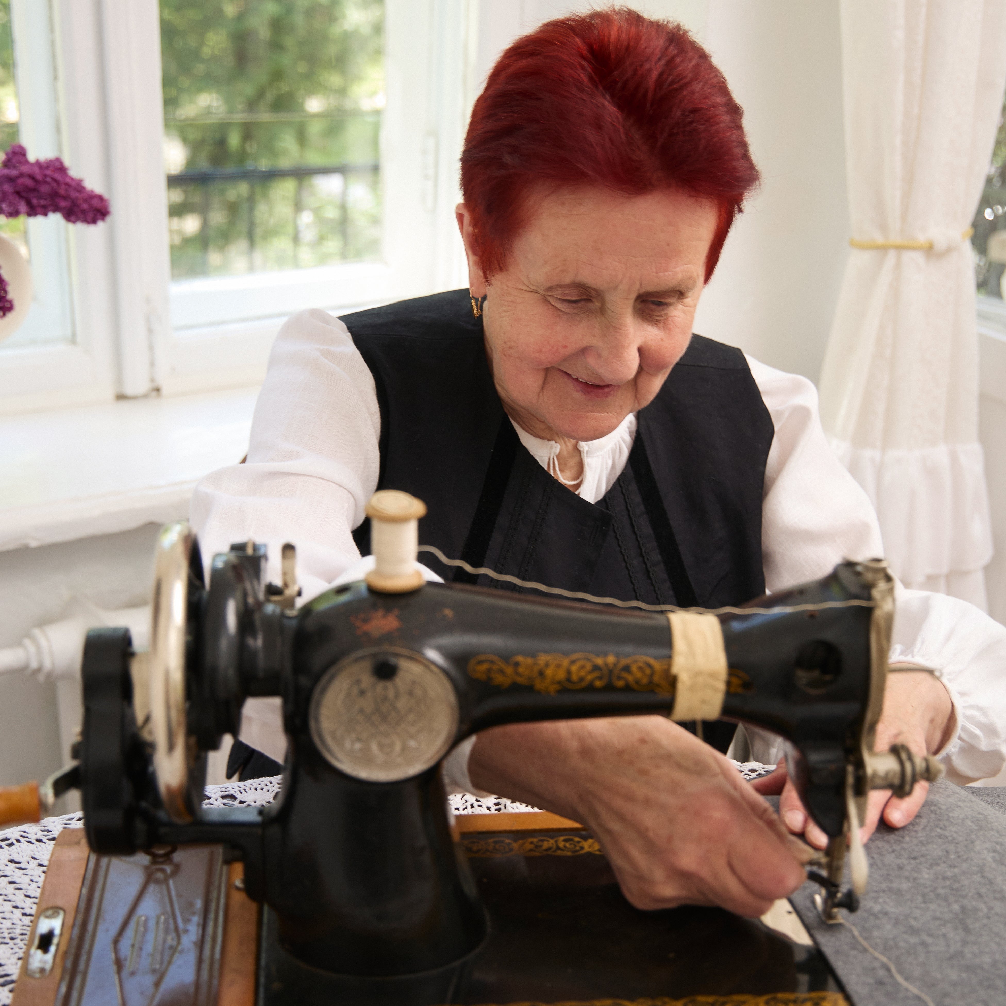 Woman with red hair operating an old-fashioned sewing machine indoors.