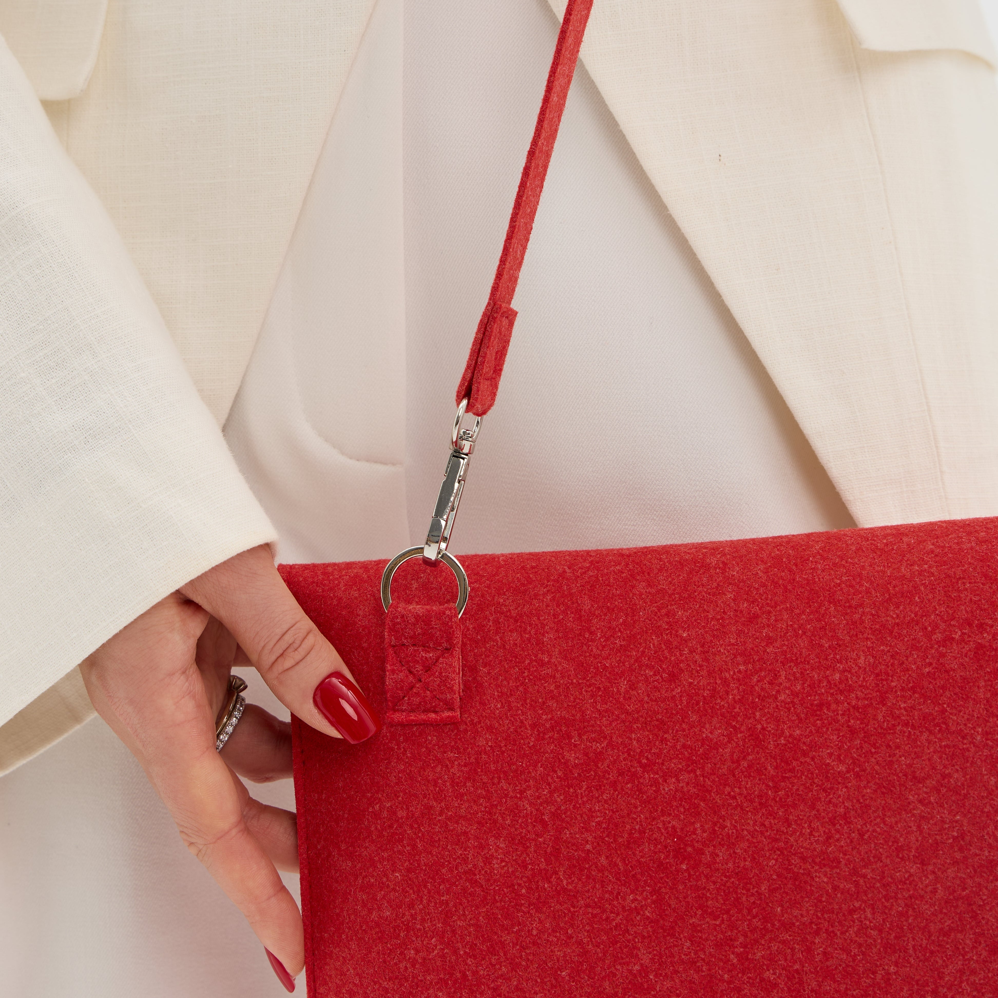 Red bag held by a hand with red nail polish, wearing a beige coat.